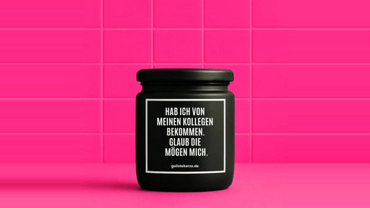 Duftkerze im Glas mit dem Aufdruck HAB ICH VON MEINEN KOLLEGEN BEKOMMEN. GLAUB DIE MÖGEN MICH, vor einer pinken Fliesenwand