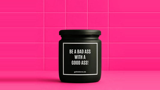 Duftkerze im Glas mit dem Aufdruck BE A BAD ASS WITH A GOOD ASS, vor einer pinken Fliesenwand