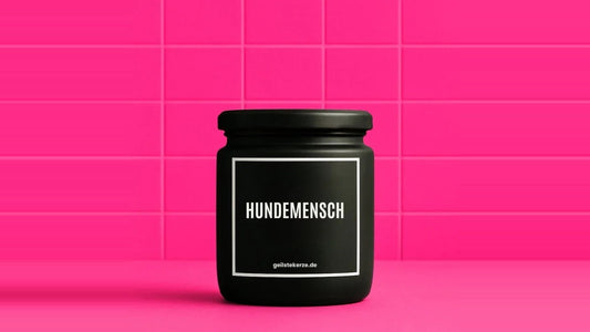 Duftkerze im Glas mit dem Aufdruck HUNDEMENSCH, vor einer pinken Fliesenwand