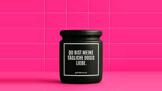 Duftkerze im Glas mit dem Aufdruck DU BIST MEINE TÄGLICHE DOSIS LIEBE, vor einer pinken Fliesenwand