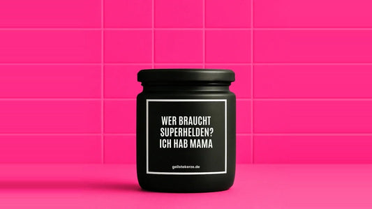 Duftkerze im Glas mit dem Aufdruck WER BRAUCHT SUPERHELDEN? ICH HAB MAMA, vor einer pinken Fliesenwand