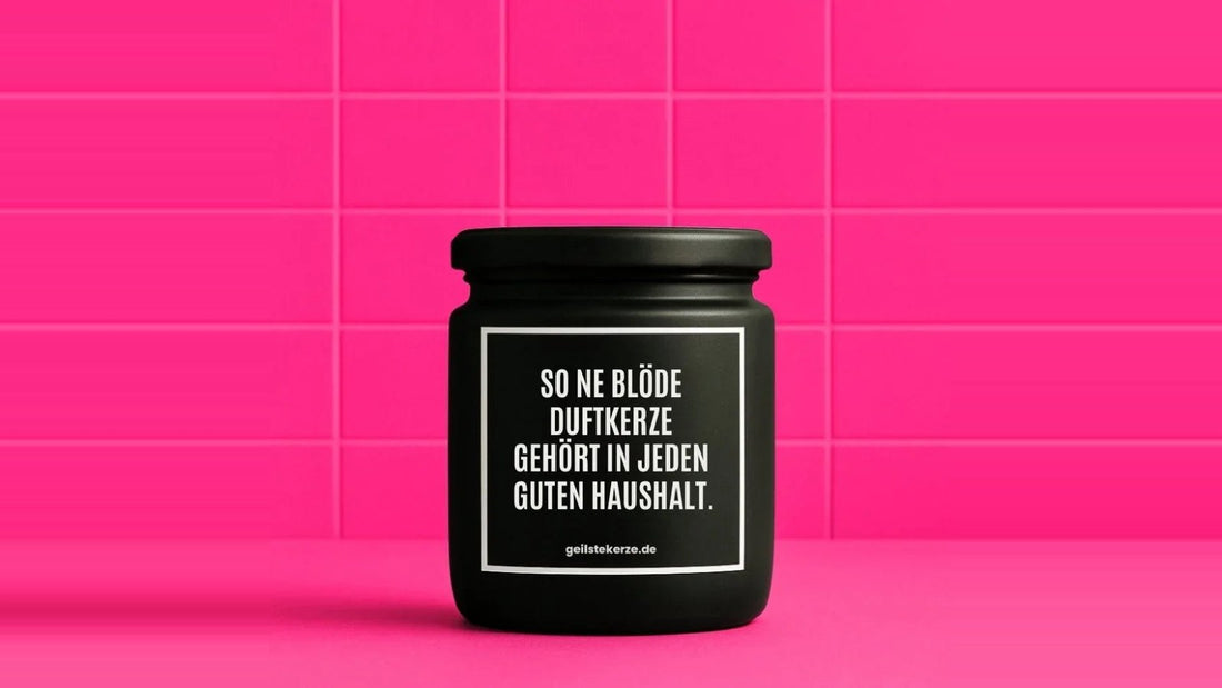 Duftkerze im Glas mit dem Aufdruck SO NE BLÖDE DUFTKERZE GEHÖRT IN JEDEN GUTEN HAUSHALT, vor einer pinken Fliesenwand