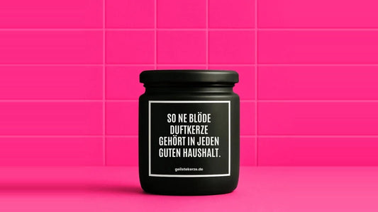 Duftkerze im Glas mit dem Aufdruck SO NE BLÖDE DUFTKERZE GEHÖRT IN JEDEN GUTEN HAUSHALT, vor einer pinken Fliesenwand