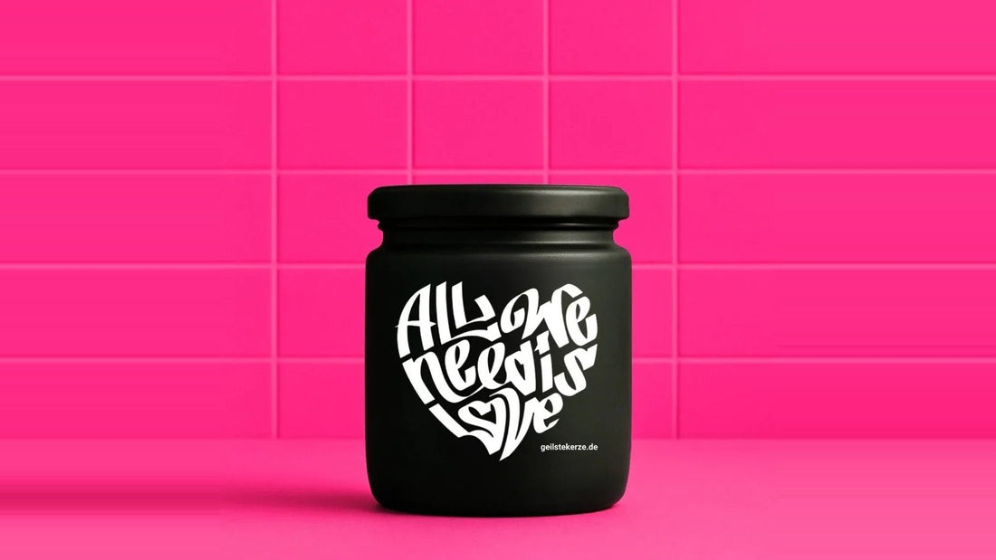 Duftkerze im Glas mit dem Aufdruck ALL WE NEED IS LOVE, vor einer pinken Fliesenwand