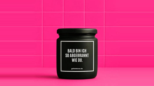 Duftkerze im Glas mit dem Aufdruck BALD BIN ICH SO ABGEBRANNT WIE DU, vor einer pinken Fliesenwand