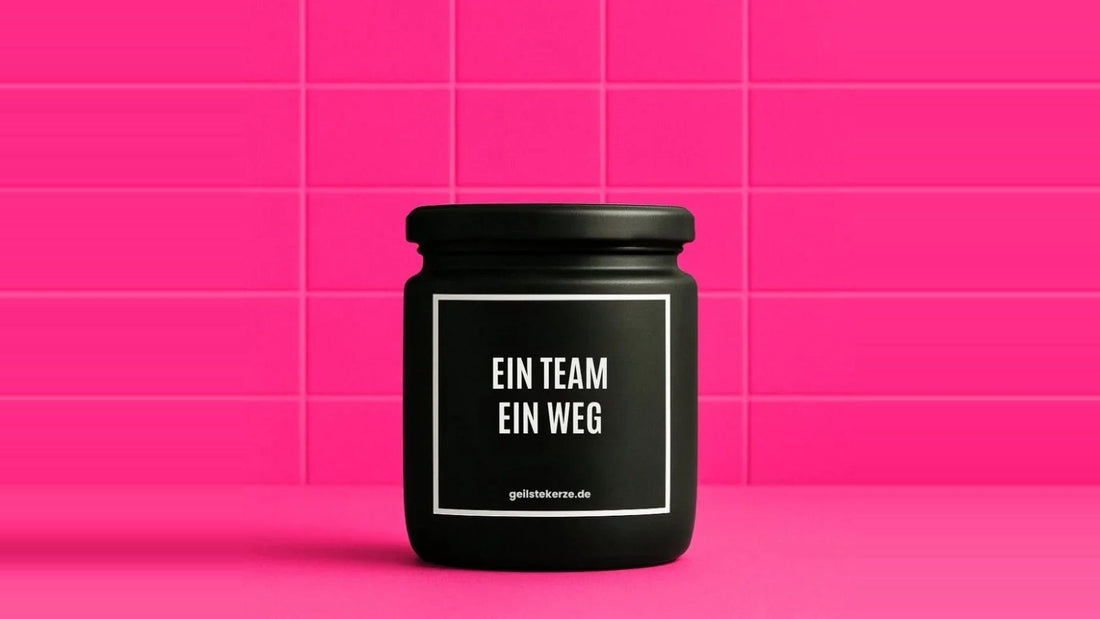 Duftkerze im Glas mit dem Aufdruck EIN TEAM EIN WEG, vor einer pinken Fliesenwand
