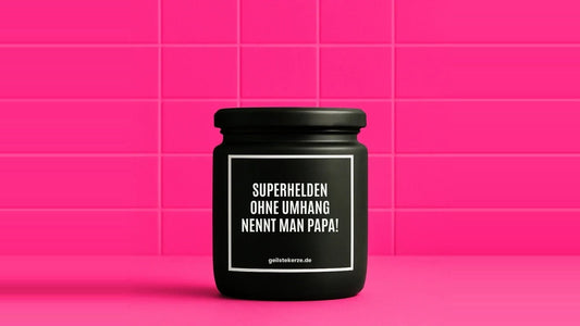 Duftkerze im Glas mit dem Aufdruck SUPERHELDEN OHNE UMHANG NENNT MAN PAPA, vor einer pinken Fliesenwand