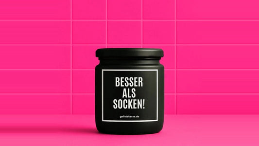 Duftkerze im Glas mit dem Aufdruck BESSER ALS SOCKEN, vor einer pinken Fliesenwand